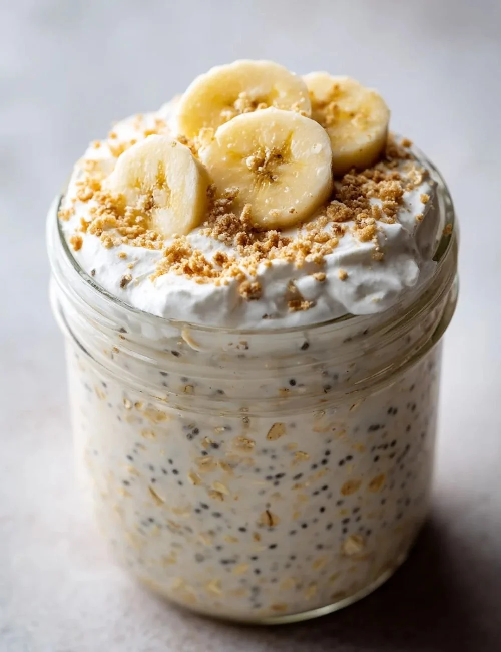 A bowl of banana cream pie overnight oats topped with sliced bananas and whipped cream.
