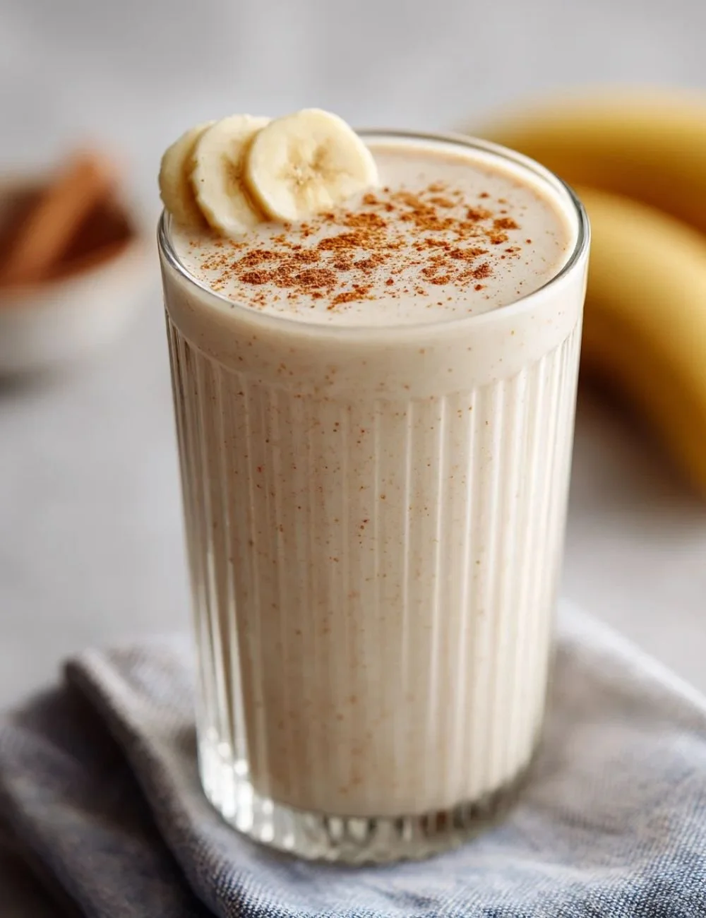 Vanilla cinnamon banana smoothie in a glass with a banana on the side