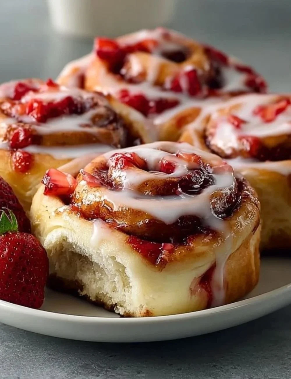 Strawberry cheesecake cinnamon rolls drizzled with icing on a plate